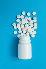 White pills pouring out of a medicine bottle on color background