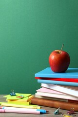 Back to school. Close-up of colorful stationery, textbooks, red apple on green chalkboard
