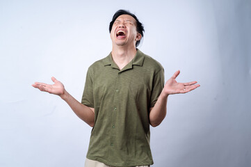 An Asian man in a green collared shirt expressing frustration or disbelief, with open arms and a distressed facial expression, standing against a plain white background in a studio setting
