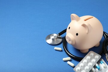 Piggy bank with stethoscope on color background. Health care financial checkup or saving for...
