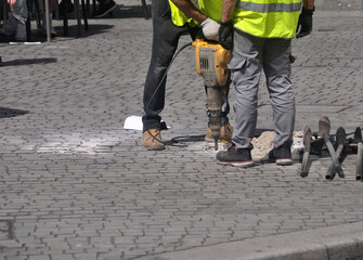 People working on a sidewalk in a city center drilling a hole with a pneumatic hammer