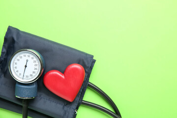 Blood pressure measuring device and heart figure on green background, top view. Space for text
