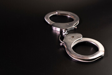 Pair of handcuffs used by law enforcement to arrest criminals on a black background. Justice or...