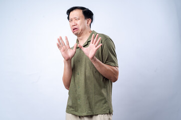 Naklejka premium An Asian man in a green shirt with a worried or disgusted facial expression, holding both hands up as if signaling 