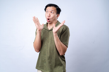 An Asian man in a green polo shirt reacts with an exaggerated surprised expression, raising both hands near his face, conveying excitement or shock, against a plain white background