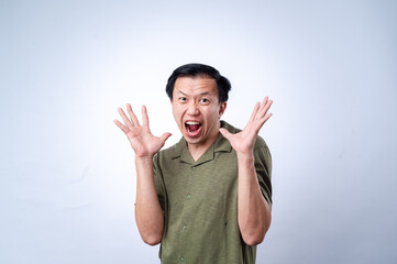 An Asian man wearing a green shirt enthusiastically raises both hands, fingers spread wide, with an...
