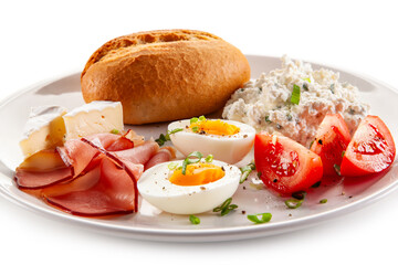 Continental breakfast - boiled eggs, white cheese, ham, tomatoes and bread roll on white background