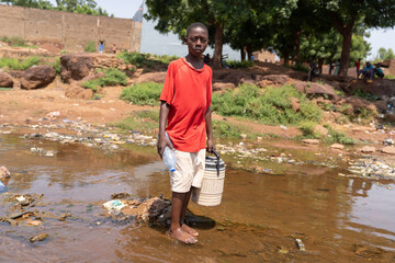 Concerned African boy with water containers searching for clean drinking water after severe storms...