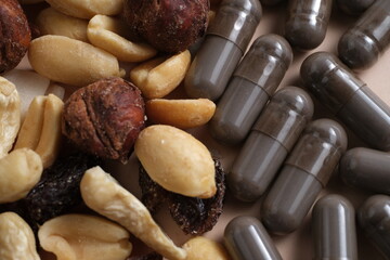 A close up view of mixed nuts and black capsules on a neutral beige background