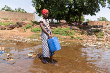 Young African woman standind with her canister in the middle of a flooded road wondering where she...
