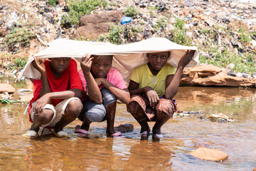 Group of African children sheltering from the bright sun under a sheet and cooling their feet in...