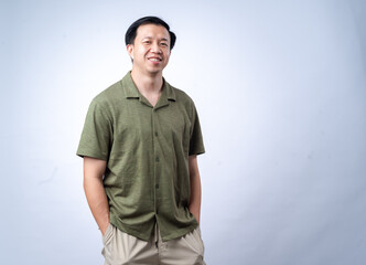 Fototapeta premium An Asian man wearing a green shirt stands confidently with his arms crossed, smiling warmly at the camera. The background is clean and white, emphasizing a professional and approachable demeanor