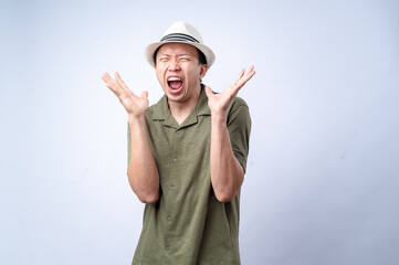 An Asian man wearing a white fedora and green shirt dramatically raises his hands in frustration, his mouth wide open as he appears to shout. He stands against a plain white background