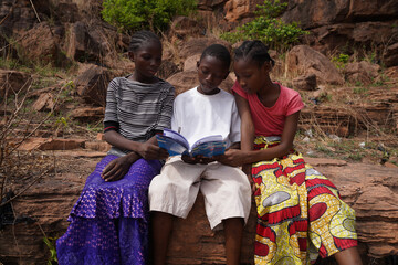 Three African village children doing their homework sharing a textbook - Concpet of lack of school...