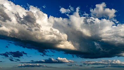 Fototapeta premium Vast clouds gather and disperse in a vibrant blue sky, creating striking patterns and shapes in the late afternoon light, showcasing nature's beauty and ever-changing weather.
