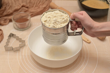 Christmas homemade baking, ingredients for baking gingerbread, woman sifting flour in a white bowl