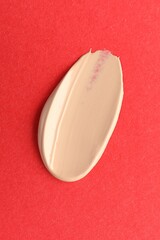 Smear of foundation on red background, top view