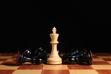 White chess king among fallen black pieces on chessboard, closeup. Competition concept