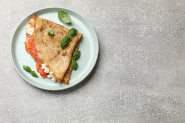 Delicious crepe with salmon, cream cheese and basil on grey table, top view. Space for text