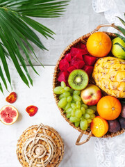 A vibrant flat-lay shot of a woven basket filled with tropical fruits, including sliced grapefruits, mangoes, pineapples, and kiwis, arranged on a bright white surface. Generative AI