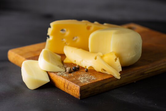 different types of cheese on wooden board on black background. Cheese product cut into pieces on cutting board