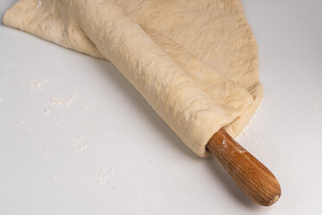 Rolled out pizza dough on a rolling pin on a white table. Pizza cooking process, recipe.