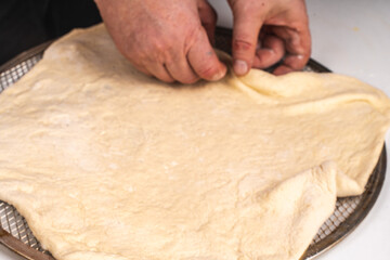 Men's hands stretching yeast pizza dough on a white table. The process of making a pizza or pie.