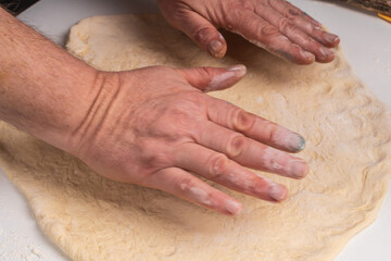 Men's hands stretching yeast pizza dough on a white table. The process of making a pizza or pie.