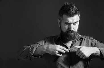 Bearded man with straight razor for shaving. Handsome barber demonstrates sharp blade of vintage straight razor. Barber shop, straight razor, bearded man. Advertising for barbershop. Black and white.