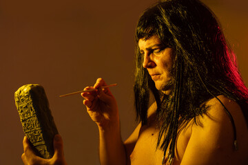 An ancient Egyptian man holds an Egyptian antiquity cuneiform clay tablet in his hands and writes...