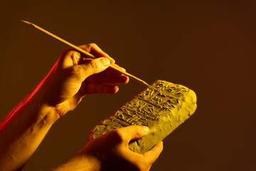 hands holding an Egyptian antiquity cuneiform clay tablet and writing ancient writings