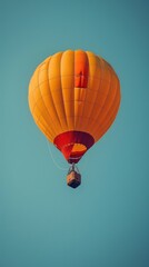 Fototapeta premium A vibrant orange hot air balloon floating against a clear blue sky.