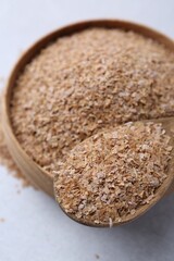 Buckwheat bran in bowl and spoon on light grey table, closeup