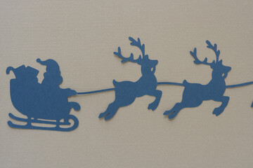 Santa and reindeers machine-cut from blue paper and arranged on a blank beige background