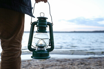 Man with vintage kerosene lamp on beach in evening, closeup