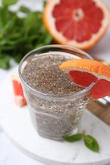 Glass of drink with chia seeds and grapefruit on white marble table, closeup