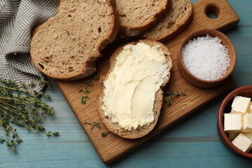 Fresh bread with butter, salt and thyme on blue wooden table, flat lay
