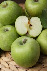 Whole and cut green apples on wicker mat, closeup
