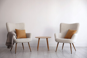 Soft armchairs and coffee table near white wall indoors