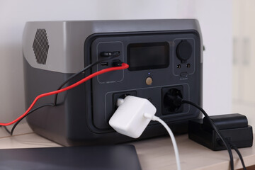 Laptop charging from portable power station on wooden table indoors