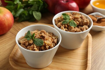 Delicious apple crisp with mint in bowls on wooden table, closeup