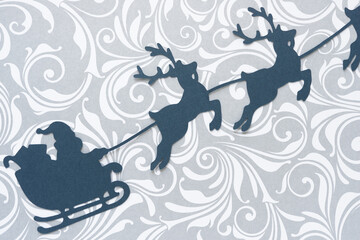 paper silhouette of Santa sleigh and flying reindeers on swirly decorative paper