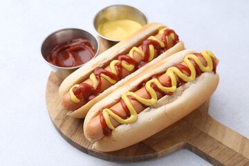Tasty hot dogs with ketchup and mustard on light table, closeup