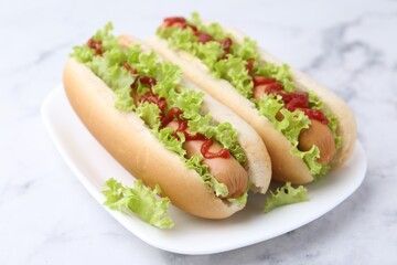 Tasty hot dogs with lettuce and ketchup on white marble table, closeup