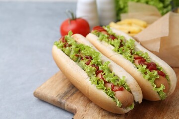 Tasty hot dogs with lettuce, ketchup and potato fries on light grey table, closeup