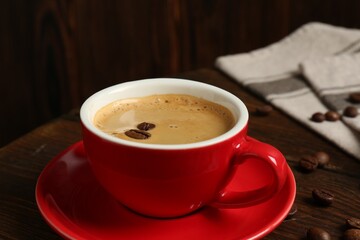 Red cup with coffee and roasted beans on wooden table, closeup