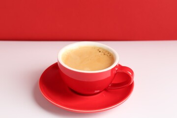 Red cup with coffee on white table, closeup