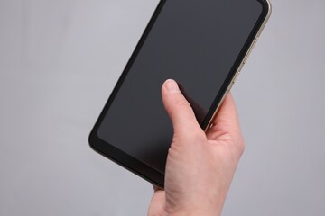 Woman using smartphone with blank screen on grey background, closeup