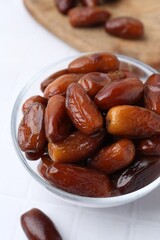 Tasty dried dates in glass bowl on white table, closeup