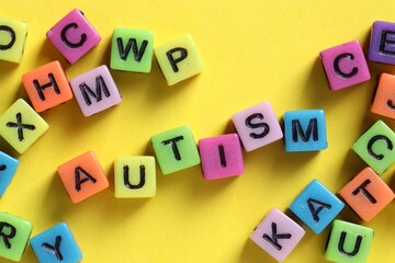 Word Autism made with colorful cubes on yellow background, flat lay